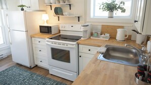 Una cocina compacta con electrodomésticos blancos, encimera de madera y una ventana con una planta.