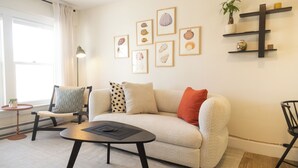 Una sala de estar con un sofá, una mesa de centro, una silla, una lámpara de pie y una pared decorada con marcos.