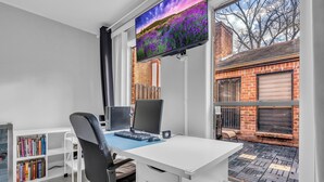 Escritório moderno com uma grande escrivaninha, dois monitores, uma estante e uma TV exibindo um campo de flores roxas.