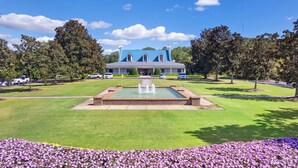 A large building with a blue roof, a central fountain, and a well-maintained lawn with purple flowers.