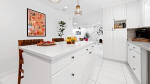 Une cuisine moderne avec des meubles blancs, un îlot central et des luminaires suspendus.