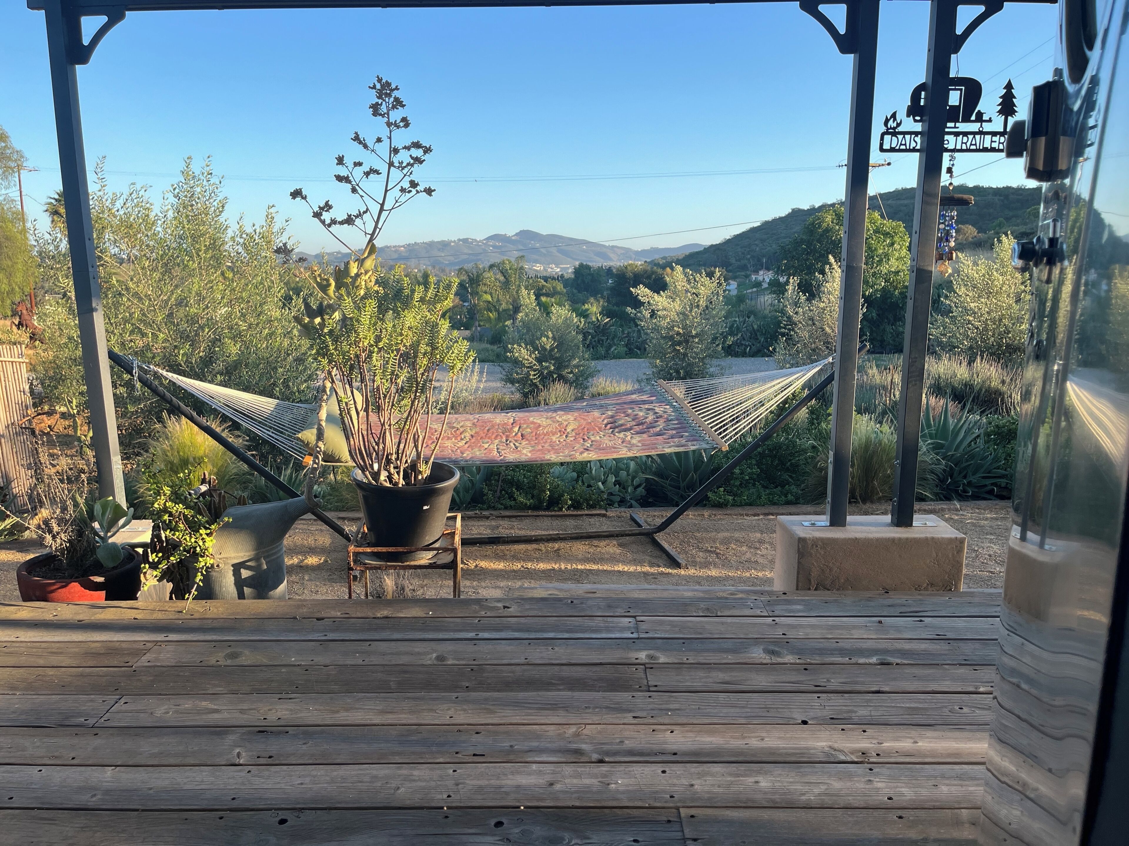A wooden deck with a hammock, potted plants, and a view of a mountainous landscape.