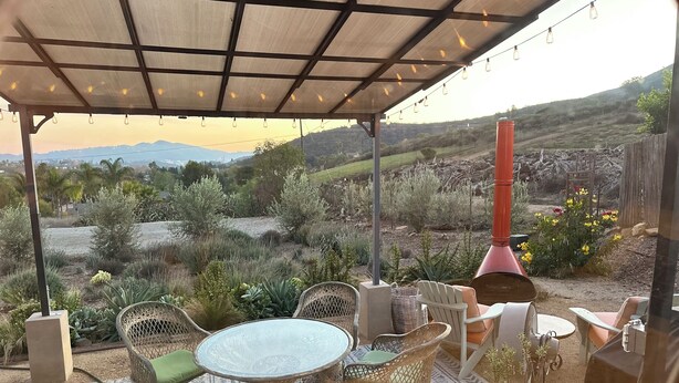 Un patio al aire libre con mobiliario de mimbre, una mesa redonda y vistas a un paisaje natural.