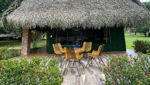 Une construction à toit de chaume comprenant un espace repas avec des chaises et une table en osier.