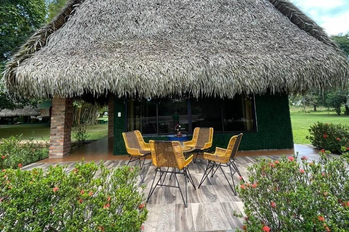 A thatched-roof structure with a dining area featuring wicker chairs and a table.