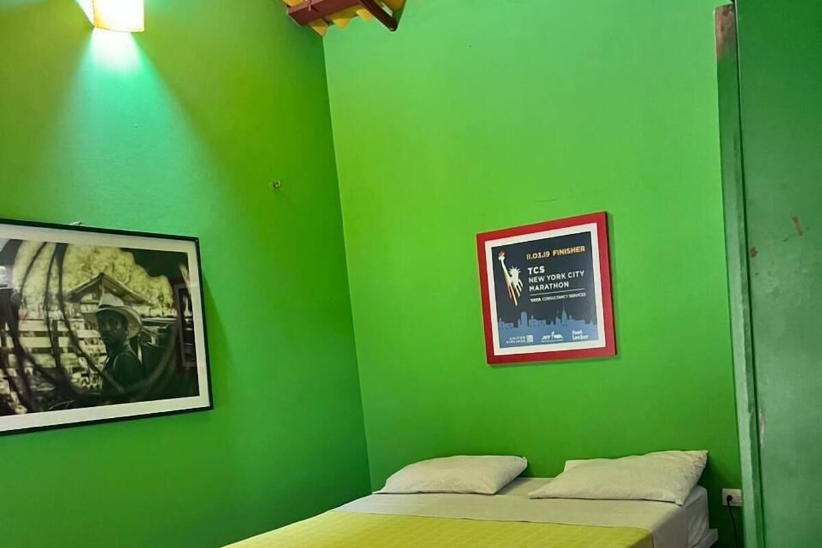 A room with green walls, a bed with a yellow bedspread, a framed certificate on the wall, and a small rug.