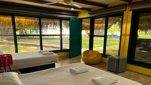 Une chambre d’hôtel avec deux lits, un fauteuil rouge, un pouf jaune et un petit radiateur.