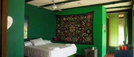 Una habitación con cama, un tapiz, ventilador de techo y una ventana con cortinas.