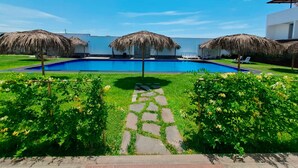 A swimming pool with thatched umbrellas, a stone pathway, and lush greenery. - HOTEL KENDARI (Grocio Prado)