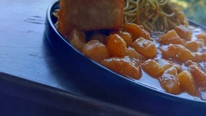 A plate of food with a piece of meat and noodles, set on a table with a view of a pool and umbrellas. - HOTEL KENDARI (Grocio Prado)