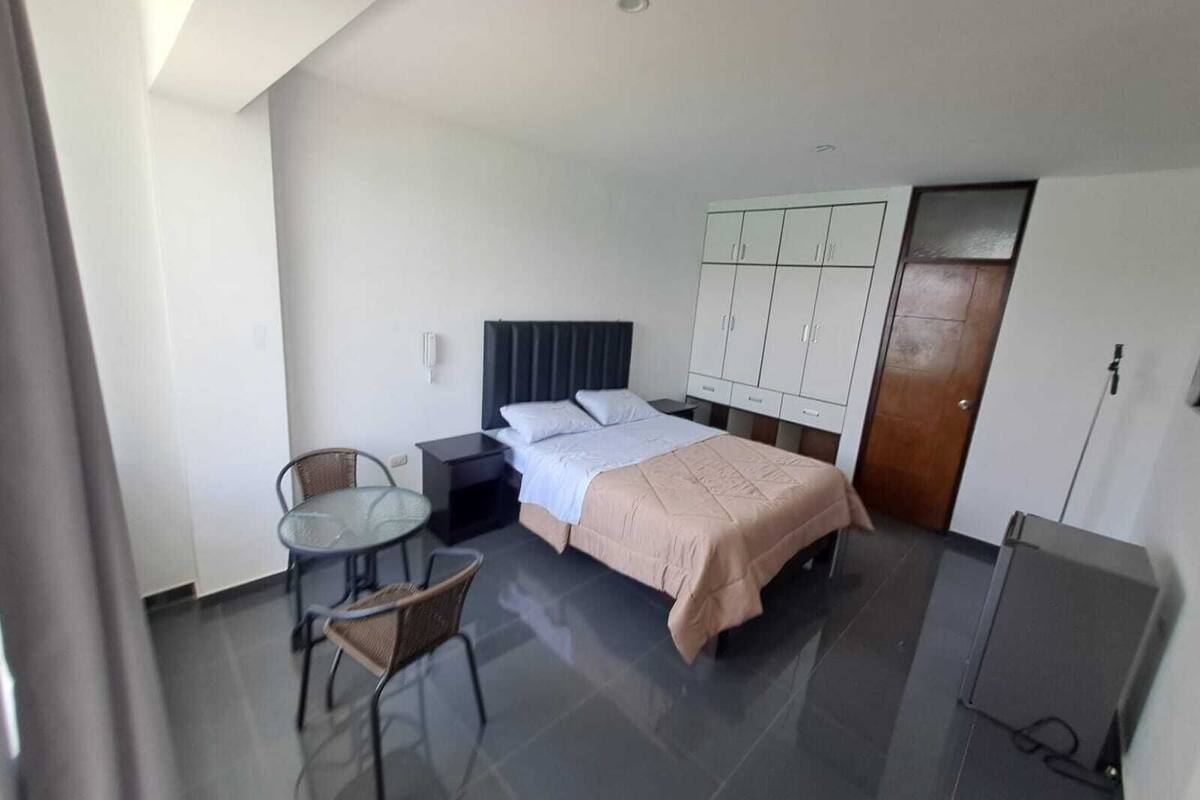 A hotel room with a bed, a small table with chairs, a wardrobe, and a door.