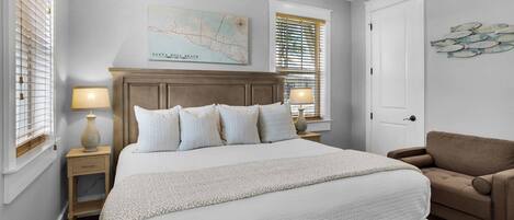 A bedroom with a large bed, two bedside tables with lamps, a ceiling fan, a map on the wall, and a door.