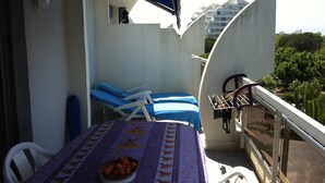 A balcony with a table set with a bowl of fruit, two lounge chairs, and a drying rack. - Rent apartment in la grande Motte, couchant district with air conditioning (La Grande-Motte)