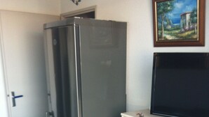 A compact kitchen with a stainless steel refrigerator, a television on a cabinet, and a door leading to another room. - Rent apartment in la grande Motte, couchant district with air conditioning (La Grande-Motte)