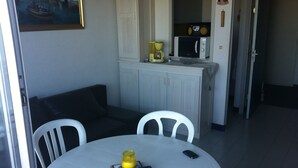 A small dining area with a round table, two white chairs, a black couch, and a kitchen area with a microwave and coffee maker. - Rent apartment in la grande Motte, couchant district with air conditioning (La Grande-Motte)