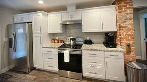Una cocina moderna con gabinetes blancos, electrodomésticos de acero inoxidable, encimeras de granito y una pared decorativa de ladrillo.