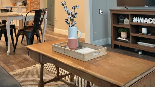 Una sala de estar moderna con una mesa de comedor de madera, sillas, un mueble para televisión y una cocina al fondo.