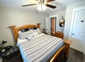A bedroom with a bed, a ceiling fan, a nightstand, a dresser, and a door. - LadyFace Cottage: close to Magnolia & Baylor! (Waco)
