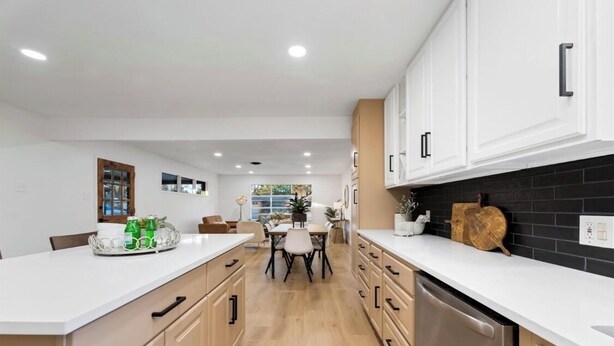 A modern kitchen with white cabinets, a central island, and a dining area with a table and chairs.