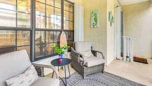 A sunlit room with wicker furniture, a potted plant, and a surfboard leaning against the wall. - Walk to Pool & Beach: PCB Resort Getaway w/ Porch (Panama City Beach)