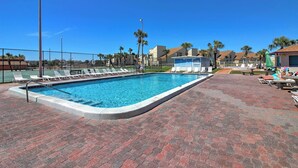 A swimming pool with lounge chairs and a covered area, surrounded by palm trees and buildings. - Walk to Pool & Beach: PCB Resort Getaway w/ Porch (Panama City Beach)