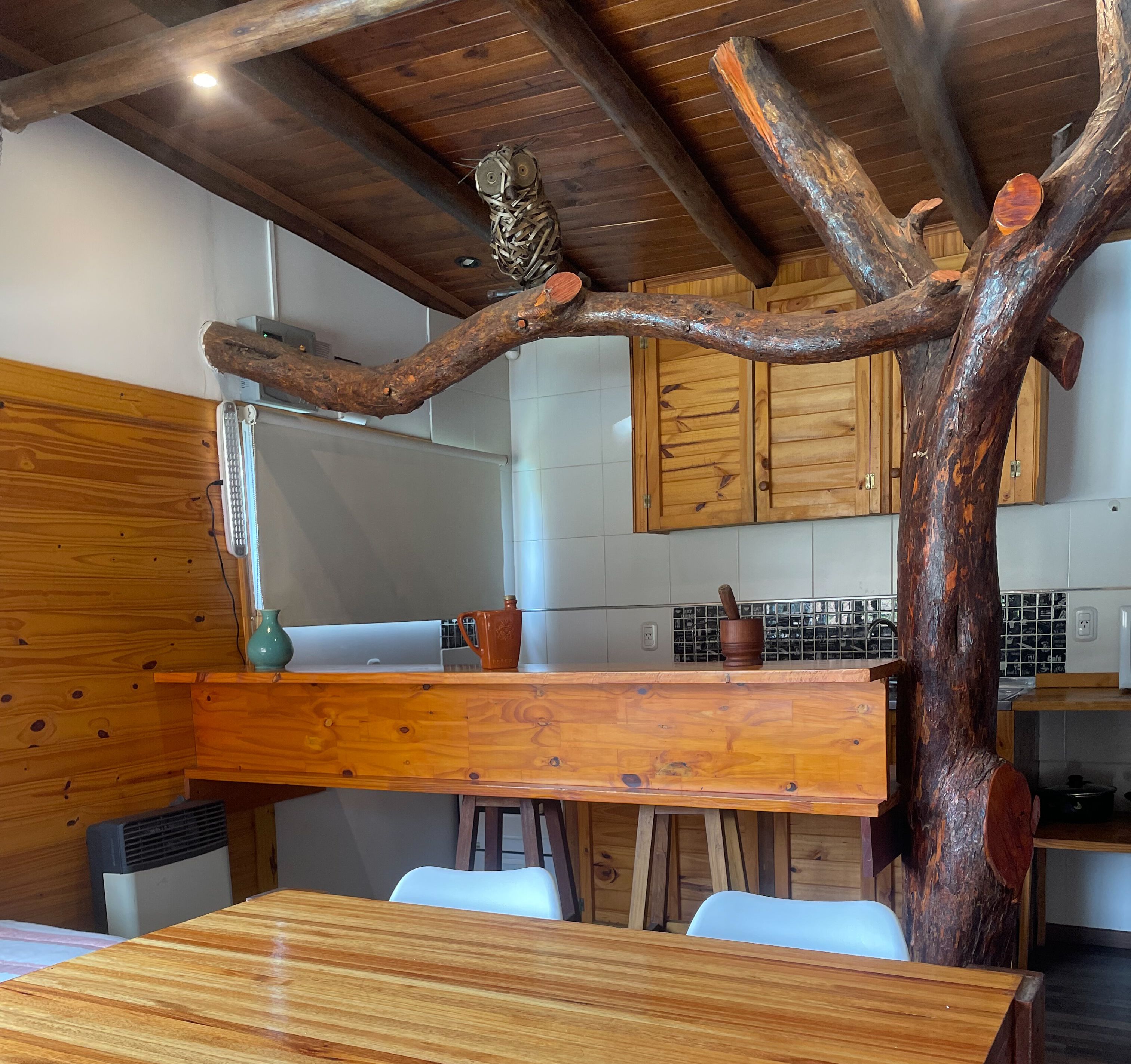 Une cuisine rustique avec des meubles de rangement en bois, une table à manger en bois et une structure originale faite de branches d’arbre.