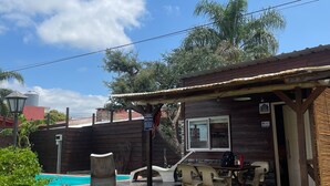 A rustic wooden building with a covered patio, outdoor seating, and a view of the sky and trees. - Vivisierras Espectacular Cabaña Villa Carlos Paz pileta privada barrio exquisito (Villa Carlos Paz)