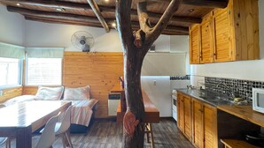 A rustic interior with exposed wooden beams, a dining area with a table and chairs, a kitchen with wooden cabinets, and a fan on the wall. - Vivisierras Espectacular Cabaña Villa Carlos Paz pileta privada barrio exquisito (Villa Carlos Paz)