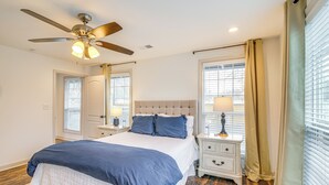 Un dormitorio con cama, mesita de noche, ventilador de techo y ventana con cortinas.