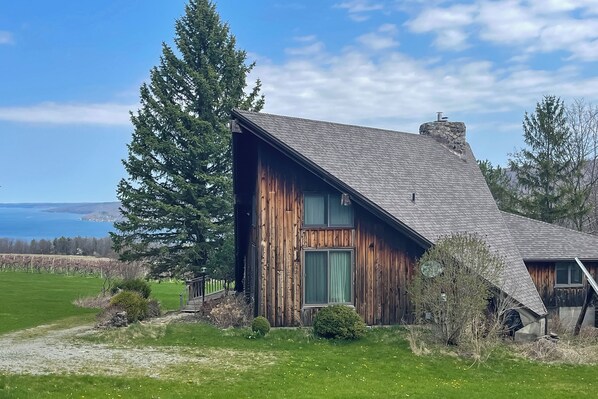 A rustic wooden house with a sloped roof, a chimney, and a view of the ocean. - Near Canandaigua Lake: Retro Cabin w/ Deck & Views (Naples)