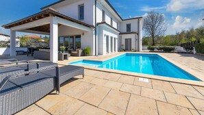 A modern house with a swimming pool, outdoor seating, and a covered patio area.