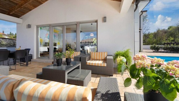 A covered outdoor patio with wicker furniture, a pool, and a view of the surrounding landscape.