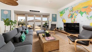A modern living room with a grey sofa, a coffee table, and a TV. There's a world map on the wall and a sign that says "SAY YES TO THE MESS".