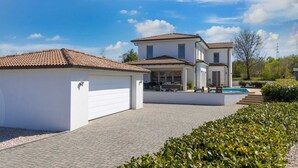 A modern two-story house with a covered patio, a swimming pool, and a well-maintained garden.
