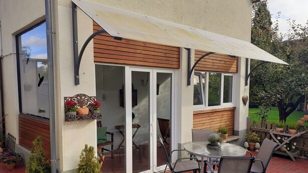 Een terras met een glazen deur, een tafel met stoelen en plantenpotten.