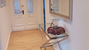 Een hal met een glazen tafel, een spiegel en twee deuren met geëtste glaspanelen.