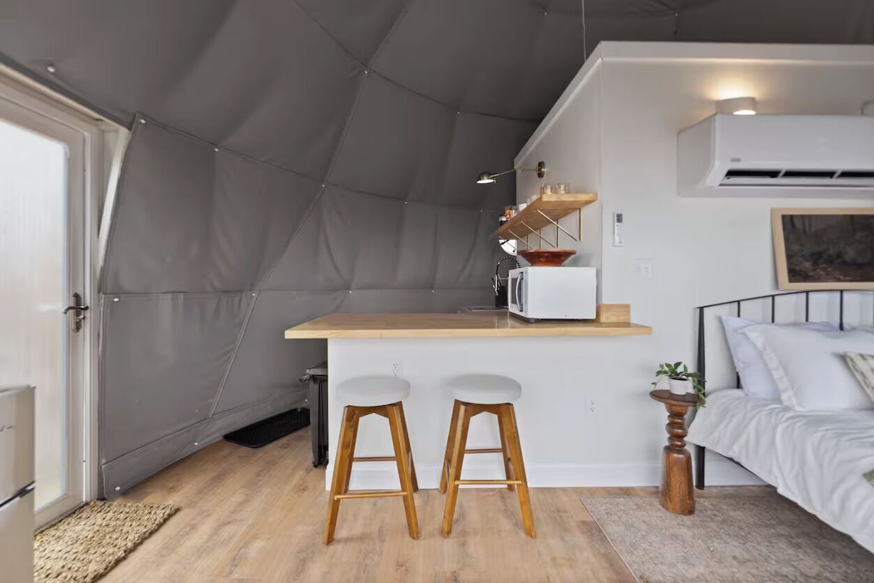A compact kitchen with a bar area, two stools, a microwave, and a small dining table.