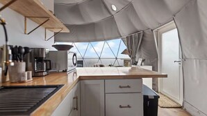 Una cucina compatta con piano di lavoro in legno, mobili bianchi e un'ampia finestra che si affaccia sul cielo.