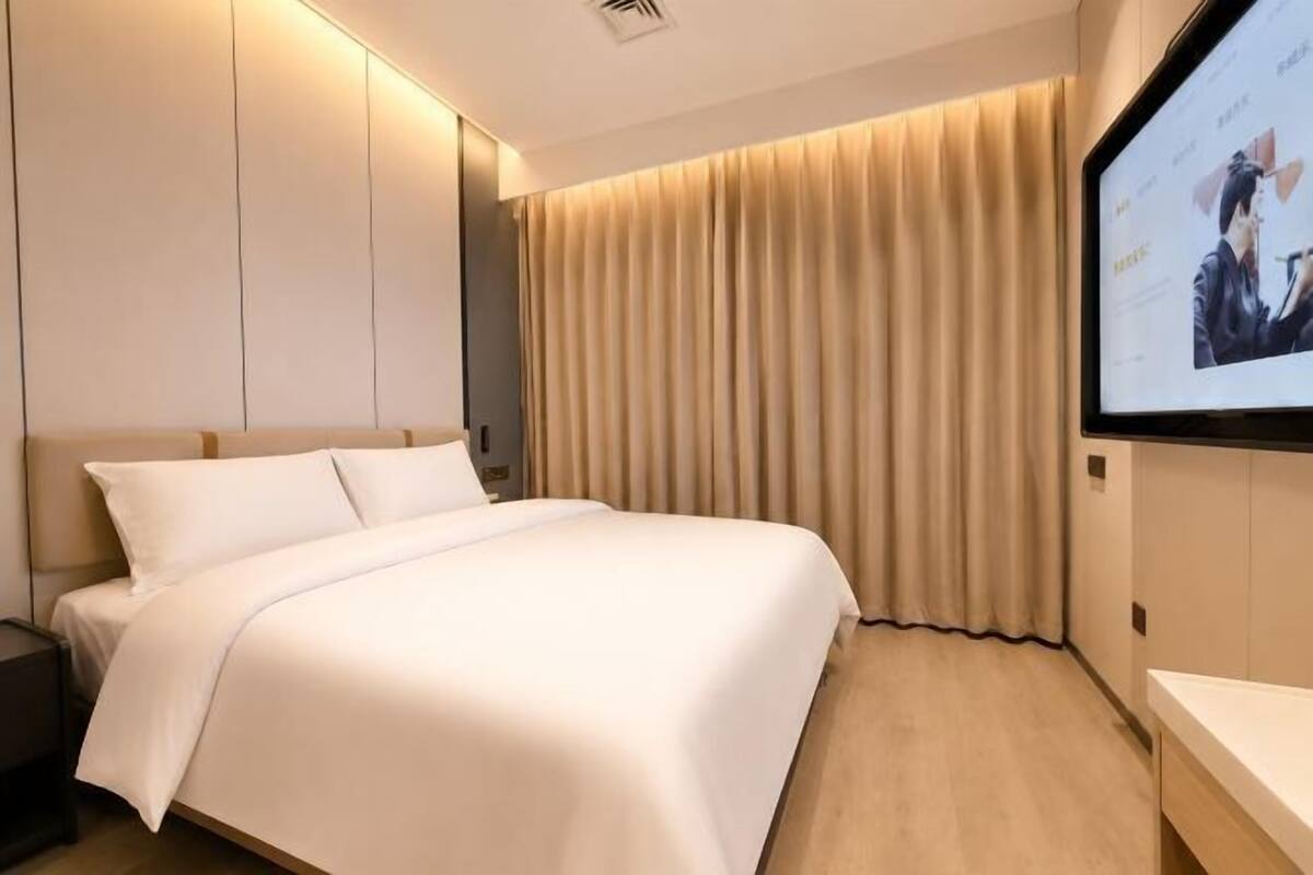 Ein Hotelzimmer mit Bett, Wandfernseher und Vorhang.