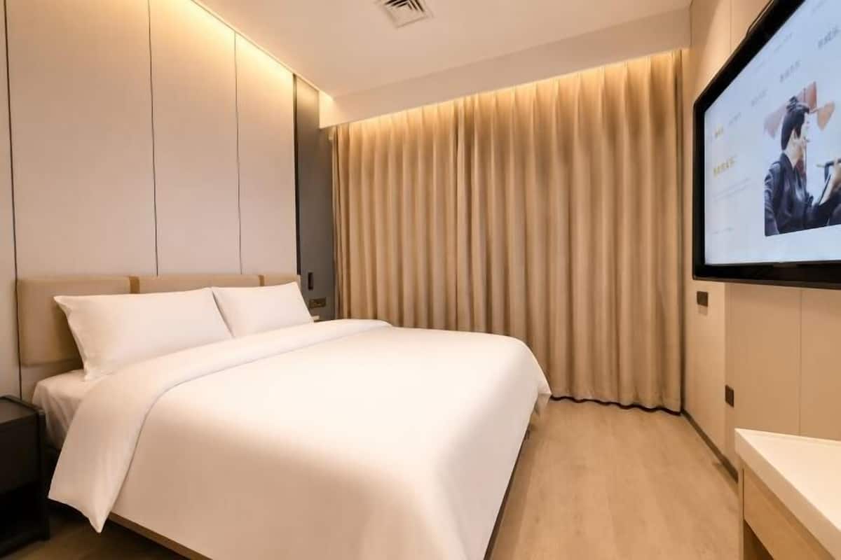 A hotel room with a bed, a TV mounted on the wall, and a curtain.