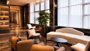 A modern lobby with a sofa, chairs, a coffee table, a reception desk, and a large plant. - Beijing Baishang Hotel (Beijing)
