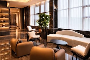 Een moderne lobby met een bank, stoelen, een bijzettafeltje, een receptiebalie en een grote plant.