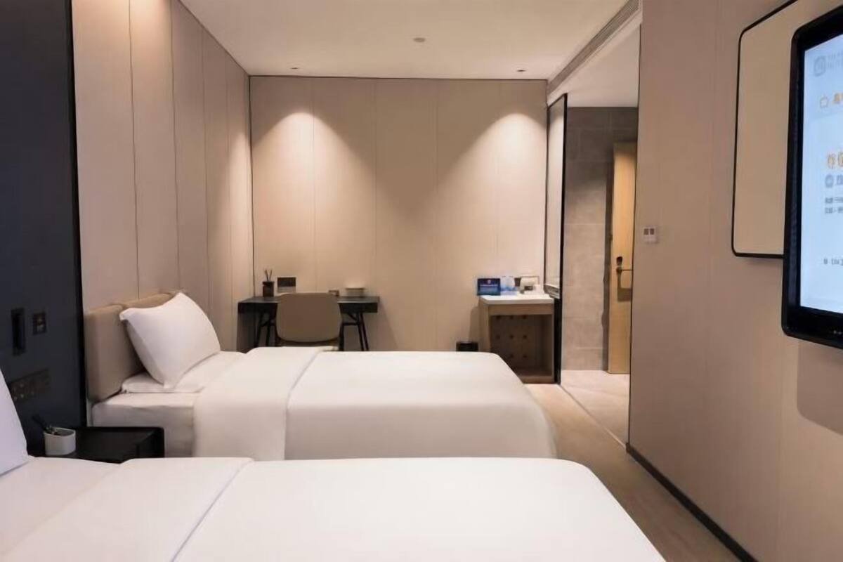 Ein Hotelzimmer mit zwei Betten, einem Schreibtisch, einem Sessel, einem kleinen Tisch und einem Fernseher.
