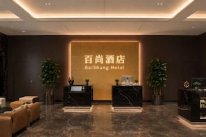 Een hotel receptie met een marmeren vloer, twee balies en een groot bord met de naam van het hotel.