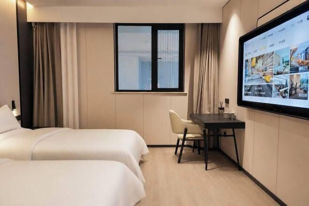 Ein Hotelzimmer mit zwei Betten, einem Schreibtisch, einem Sessel, einem Fernseher und einem Fenster mit Vorhängen.