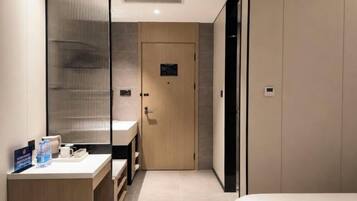 Una habitación de hotel moderna con una puerta de madera, una mesita de noche pequeña con una taza y una botella, y un espejo grande.