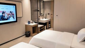 Habitación de hotel con cama, escritorio, computadora, espejo y televisor.