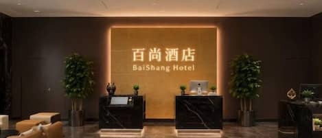 A hotel reception area with a reception desk, seating area, and a large sign displaying the hotel name.