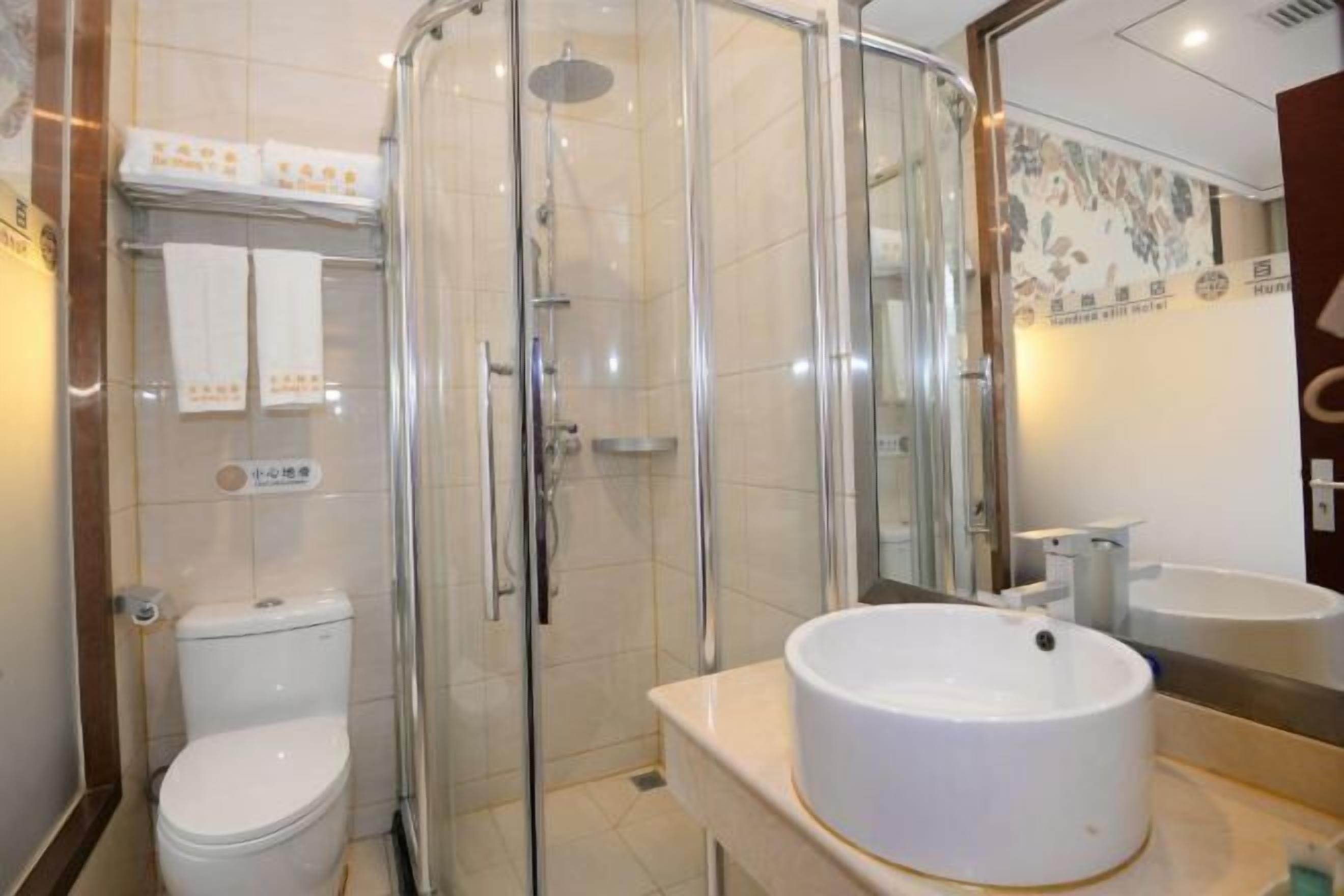 Een moderne badkamer met een douchecabine van glas, een wit toilet en een rond wastafeltje met een spiegel erboven.