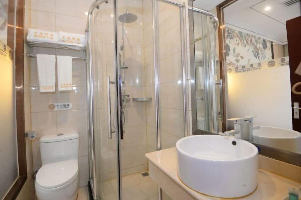 Ein modernes Badezimmer mit einer einachigen Duschkabine, einer weißen Toilette und einem runden Waschbecken mit Spiegel darüber.